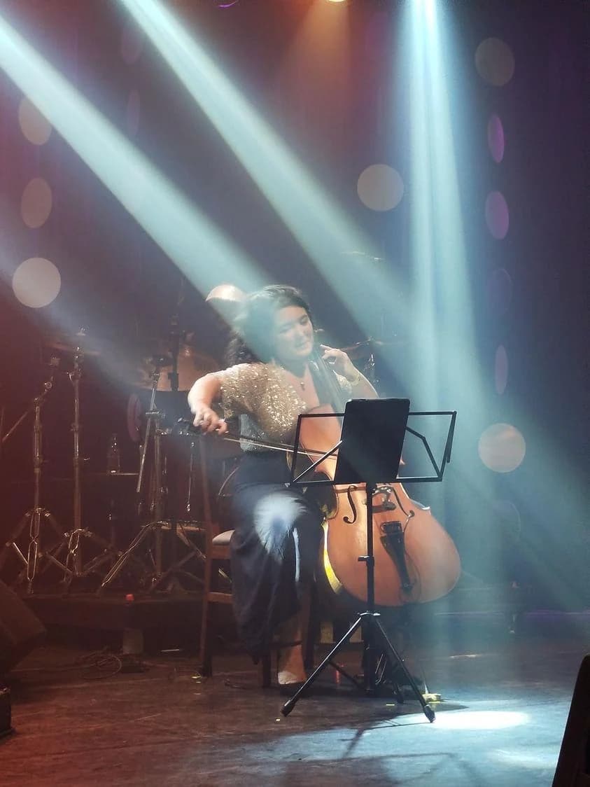 Stephanie playing cello under stage light beams